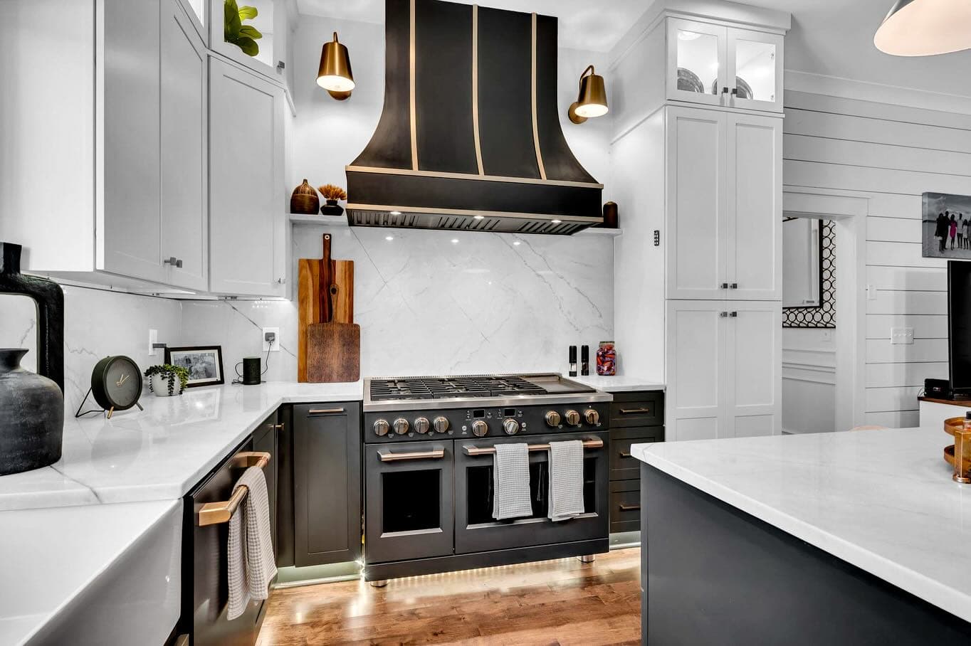 Black and brass range hood over a professional range with marble backsplash